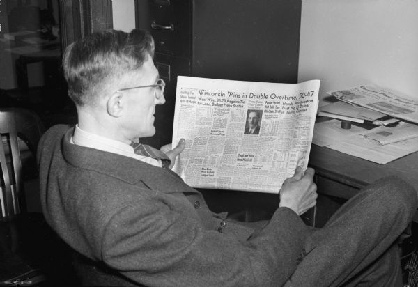 Phil "Scoop" Wackman, Brooklyn village banker. He is reading a newspaper with a headline that reads: "Wisconsin Wins Double Overtime," which reminded him of the long overtime game between Brooklyn and Hazel Green High School basketball teams played in 1926; they played 12 overtime periods.