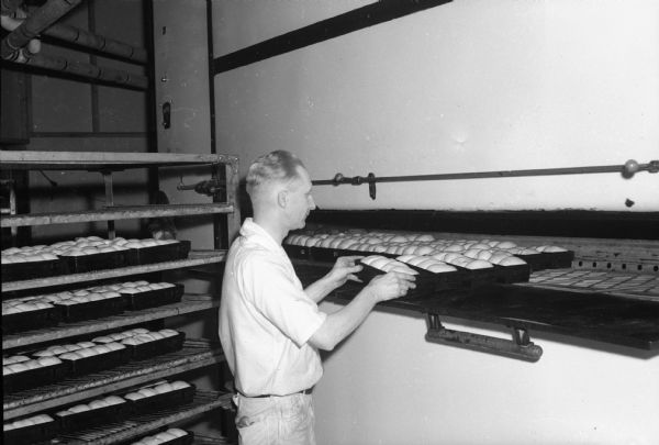 A man is putting loaves of bread in an oven at the Heilman Baking Company.