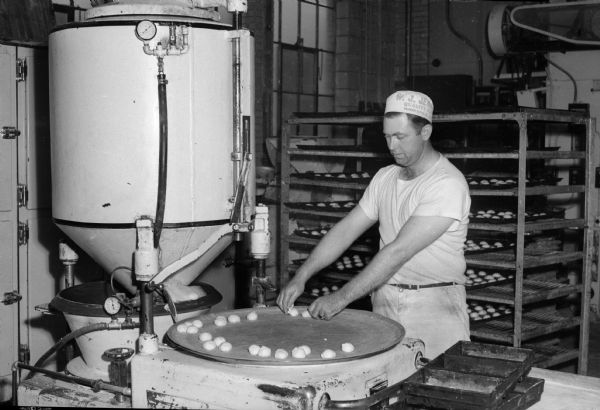 A man at the Heilman Baking Company operating a bread and bun machine that cuts dough pieces into proper sizes for bread loaves and for buns.