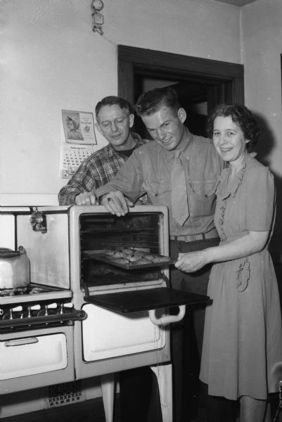 Corporal Duane Haralson with his parents, Rufus and Naomi, in the kitchen of their home at 604 Schiller Court. He was home after two years service in the Marine Corps. Naomi is taking cookies out of the oven.