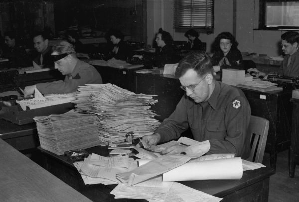 Private George Grasser, in foreground, checking in a stack of lessons which have come from soldiers and sailors at the fighting fronts of the world, for United States Armed Forces Institute (USAFI). Lessons are corrected by the University of Wisconsin-Extension.