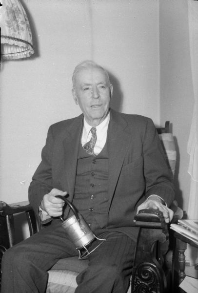 Michael G. O'Neill sitting in a chair with a railroad lantern. He lived at 526 West Wilson Street and worked 40 years for the Milwaukee Road.