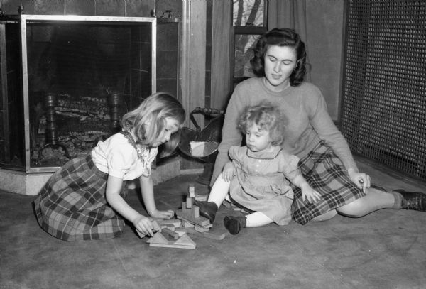 Betty Frey, student at the University of Wisconsin, and two children, Geraldine Myers and Barrie Anderson, playing in a nursery school established on the third floor of the home of University president, Charles A. Dykstra, 130 North Prospect Avenue. Madison Nursery school was sponsored by the Junior Divison of the University League.