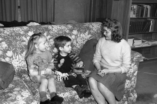 Dorothy Stebnitz, student at the University of Wisconsin, telling a story to two children, Pricilla Dee Brown and Stefan Burr, at the Dykstra House Nursery School, which was established on the third floor of the home of University president, Charles A. Dykstra, 130 North Prospect Avenue, Madison. The school was established by the Junior Division of the University League.
