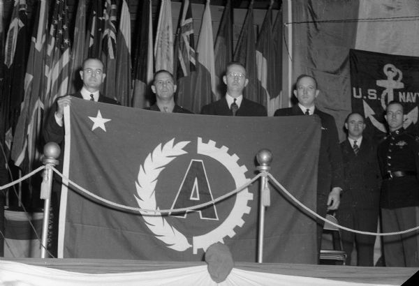 The Arlington plant of California Packing Corporation employess holding award flag. They earned an "A" achievement award for food production. Left to right are: L.S. Argall, midwest division manager of the corporation; Maj. Carl H. Hilker, Chicago quartermaster depot; Gordon Gunderson, state supervisor, office of distribution, War Food Administration; and Gordon Packard, employee representative.