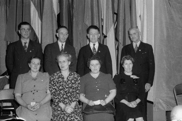 Representative employees received "A" achievement award pins at a presentation program when the Arlington plant of the California Packing Corporation received the "A" flag at the plant.  Seated, left to right, are: Mrs. Louis Bahr, Mrs. Albert Haugen, Mrs. W.W. Schultz, and Mrs. Ivan Little.  Standing, left to right are: Edwin Hummel, Arthur Sorenson, Paul Hanson, and John Delany.