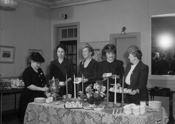 USO-Travelers Aid award ceremony tea in the Lounge and in Esther Vilas Hall of the YWCA. Standing behind the refreshment table are five volunteer workers who received awards: left to right, Grace W. Cockrell, May L. Berkowitz, Dorothy B. Lundstrom, Gussie Phil Helper, and Margaret H. Dodge.