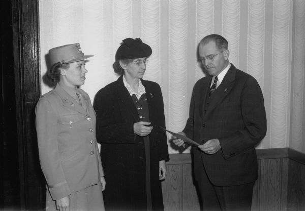 A man reading a document with two women observing, one of whom is a WAC (Women's Army Corp), at the First Congregational church, 1609 University Avenue.
