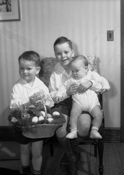 The Yaudes children, James (7 1/2), Jimmy, (3), and Tammy (7 months), children of J. Lloyd Yaudes, 2305 Rowley Avenue, with an Easter basket illustrating traditional Easter gifts for children.