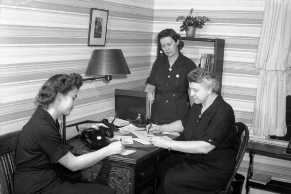 Rosemary Kreilkamp, 222 South Carroll Street, Alice Sanborn, 3005 Harvard Drive, and Ann L. Schmich, director of the Visiting Nurse Service in Madison, examining case records. Public health visiting nurses experienced heavier case loads because doctors and nurses were called to military service. The Visiting Nurse Service was located at 418 West Mifflin Street and sponsored by Attic Angel Association.