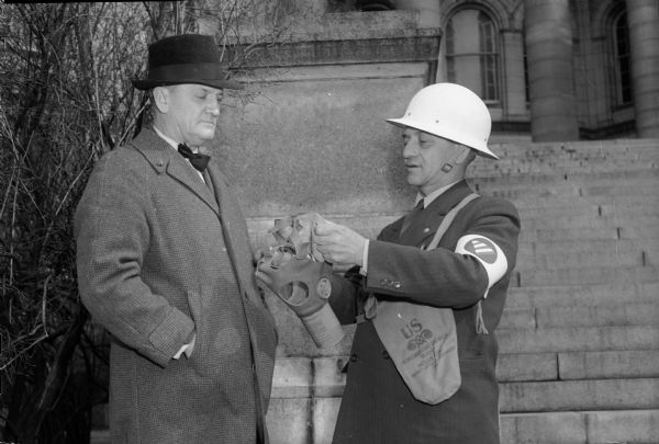 Deputy Sheriff Albert Dahle and Sheriff E.A. Fischer, chief of the air raid wardens of Dane County, demonstrating gas masks on the steps of the Wisconsin State Capitol.