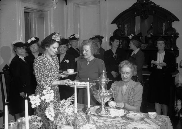 Group of women surrounding a serving table at the Silver Tea, benefiting the YWCA at the Governor's residence, 130 E. Gilman Street.