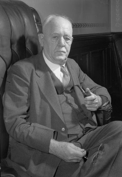 Portrait of Wisconsin Governor Walter S. Goodland, seated in a chair, holding a pipe in one hand, and his eyeglasses in the other.