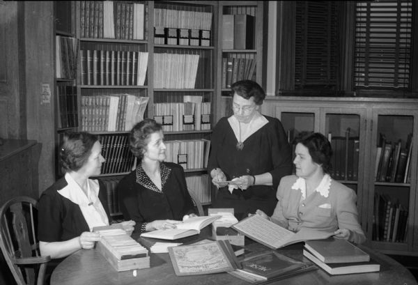 A committee of Madison women musicians, sitting around a table, selecting music books and scores to supplement the Madison Public Library collection are, left to right: E. Cath Newton, Frances Kivlin, Tahlulah Thompson, past president and chairman of the education committee of the Wisconsin Federation of Music Clubs, and Eleanor Carter.