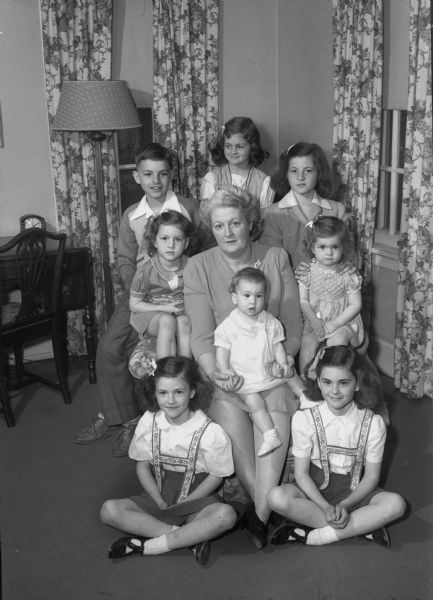 Mrs. Dorsey Botham,  (Elizabeth Botham), and her eight children: Rosemary, left, and Rosanne, right, 7 year-old twins seated on the floor; Ruth Ellen, left, age 4, and Barbara, right, age 2, seated on the arms of the chair; James, left, and Jane, right, 10 year-old twins, and Betty Lou, center, age 5, at the top of the picture; and Bridget, 10 months, seated on Mrs. Botham's lap.  The twins James and Jane had the knicknames Nip and Tuck.