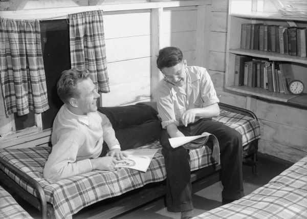 The Reverend John Clayton and Bob Clark, looking at a cartoon while sitting on a cot in the boys' hostel at the Samuel Post farm on Middleton Road.
