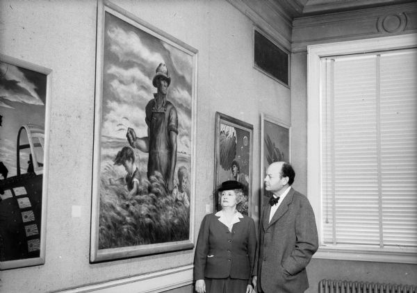 Mrs. Walter Goodland (wife of Governor Goodland), and John Steuart Curry standing in front of "Our Good Earth," by John Steuart Curry at a Memorial Union exhibit of paintings executed for use on war posters.