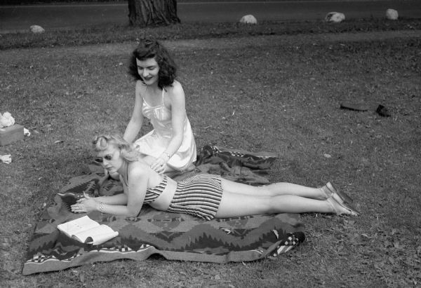 Pat Stevens is lying on her stomach, and Donna Arnold is checking her for the first signs of angry red indicating the first stages of a sunburn.