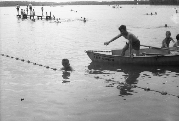 Lifeguard Tom Langlois in a rowboat is issuing a warning to James Bergman who is swimming outside the ropes that delineate the safe swimming area.