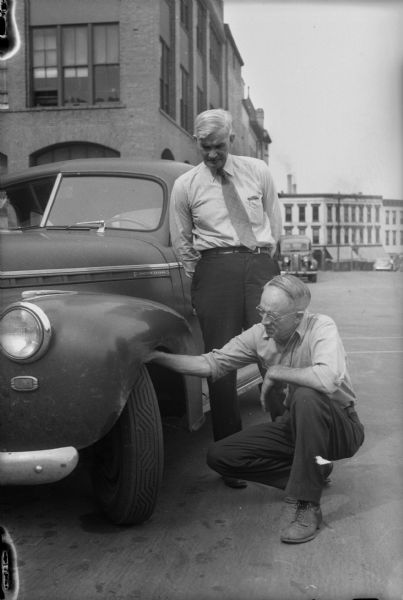 Two men looking at an automobile's tires at Monona Tire Company, 128 South Pinckney Street.