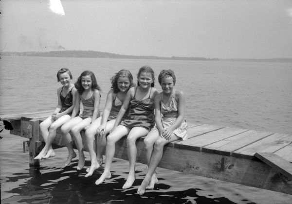 Five girls sitting on a pier on Lake Mendota at YWCA's Camp Maria Olbrich. From left to right:  Edith Gannon, Sally Smith, Mary Ellen Segerson, Turabelle Olson, and Elspeth Hughes.