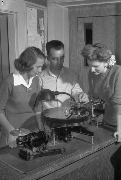 Three persons at the summer radio workshop sponsored by WHA Radio on the University of Wisconsin campus. Jack Steel shows Senta Lorenz on the left and Ruth Alexander on the right how to make an electrical transcription.