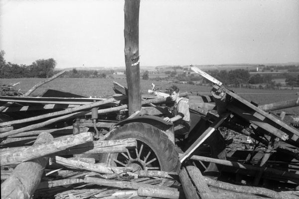 Truax Field tornado damage, 2 miles north of Truax Field. Francis Lockman, son of Mr. and Mrs. Everett Lockman, is sitting on the seat of their tractor which is buried in the remains of a tobacco shed, with its timbers piled up by the wind.