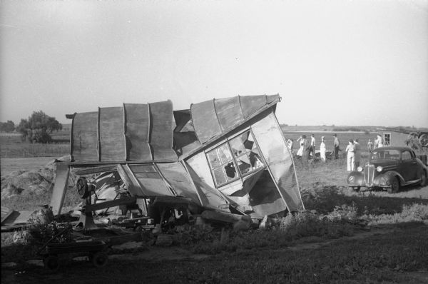 Tornado damage near Truax Field in Madison. The Gritzmacher farm milk house was twisted and shattered by the wind. A group of people are looking at the damage.
