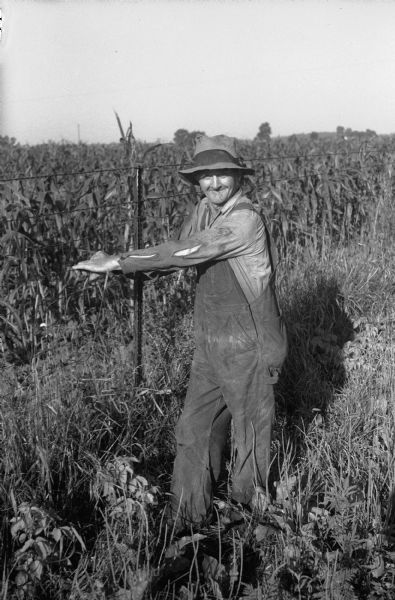 Tornado damage in Truax Field area. Albert Anderson is shown holding the wire of a fence that held him during the storm. Oscar and Elmer Anderson, Albert's brothers, were with him during the storm.