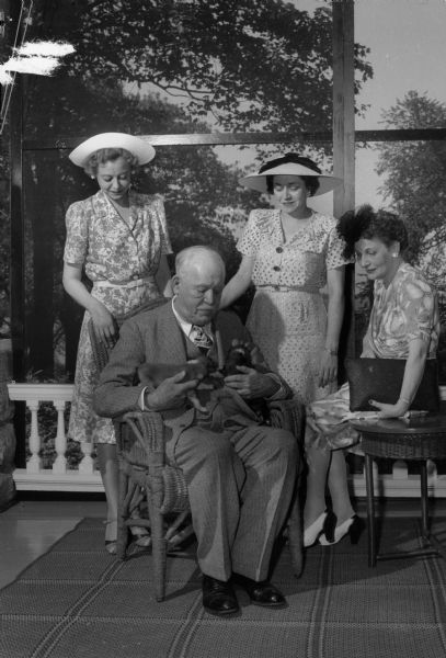Governor Walter Goodland is holding two of ten puppies during the League of Women Voters garden party at the Governor's Residence. Shown with the Governor are Florence Bratlie, Lucille O'Keefe and Alice Hammes. Bratlie was employed in the main office of the public service commission, O'Keefe was office manager of the Wisconsin Alumni Research Foundation, and Hammes was secretary to the state director of safety.