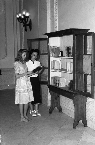 Students Dorothy Vecke, Milwaukee, and Kuo Chung-Ying, China, examine the bookcase that was the original Wisconsin State Historical Society library of the 1850's. The bookshelf formerly resided outside the library on the second floor of the Wisconsin Historical Society at 816 State Street.