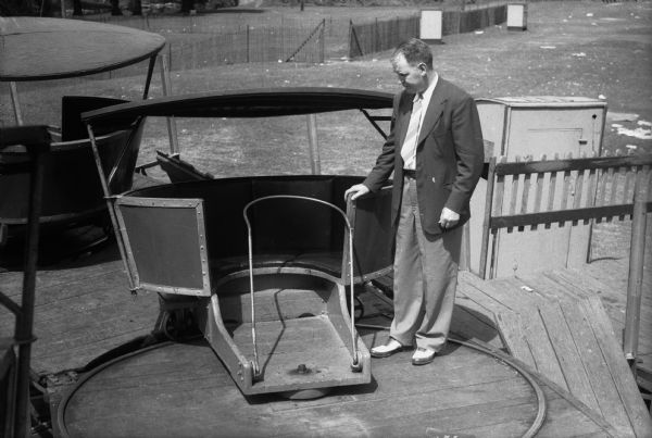 John J. Walsh, Madison attorney-at-law, standing next to the Tilt-a-Whirl ride at the Madison East Side Festival, the scene of an accident in which a teenage girl, Lois Bailey, was thrown from the ride.