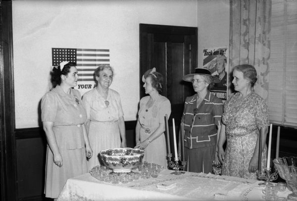 Five members of the Madison Woman's Club.  Left to right, Mrs. H.J.  (Dorothy) Schubert, Mrs. L.L. (Gertrude) North, Mrs. C.K. (Helen) Schubert, Mrs. George (Flora) Ritter, and Mrs. Howard (Clara) Piper. They are standing around a punch bowl on a table decorated in a red, white, and blue motif.
