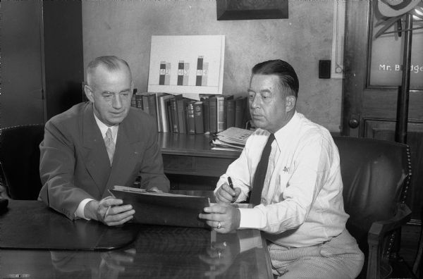 Two men at a desk at the National Mutual Benefit Insurance Company.