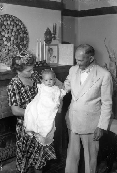 Group portrait showing christening of Richard Upson. From left: Pat Upson, wife of Lieutenent Commander Richard Upson, holding her ten month old son, Richard, and the Reverend E.D. Upson, grandfather of the baby. The Reverend Upson performed the christening in the Upson home. The baby's father is missing in action overseas.