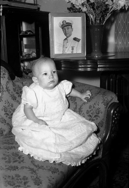 Richard Upson, ten-months-old, with portrait of his father in background, Lieutenant Commander Richard Upson, who is missing in action overseas.