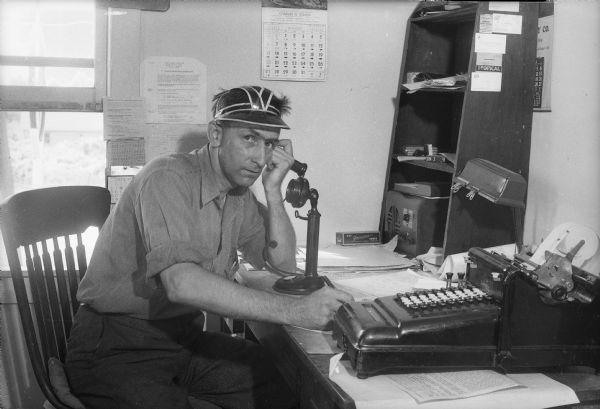 O.C. Harris talking on the telephone in the office of his business, which is the O.C. Harris Company, 1217 East Broadway, Dane County's only twenty-four hour a day emergency highway service.