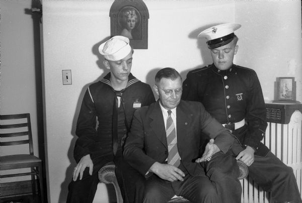 Charles W. Piper, veteran of World War I, discussing tactics of the two World Wars with his sons, Seaman Vincent on the left, and Marine Private Charles on the right.
