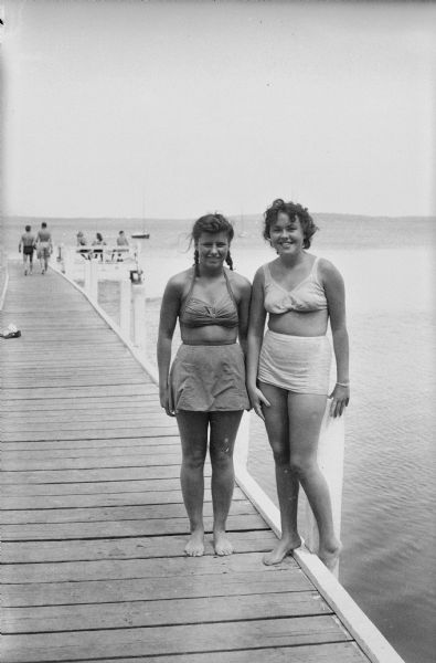Two women in bathing suits standing on pier.