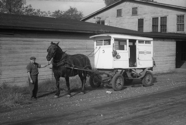 Milkman from Kennedy-Mansfield Dairy posed next to horse-drawn delivery wagon, number 5, and the horse.  This photograph documented a story about the end of the era for milk delivery using horse-drawn wagons.