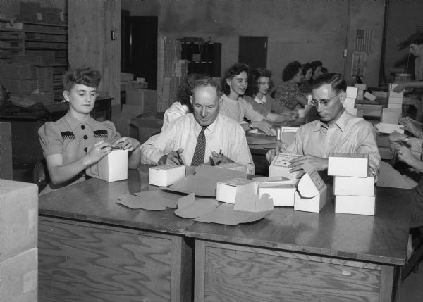 Lois Wiessinger, Michael Mack, and Harold Stone, state employees, filled 21,600 Christmas packages to be sent by the American Red Cross to hospitalized servicemen overseas. The photograph was taken in the basement of the State Office Building.