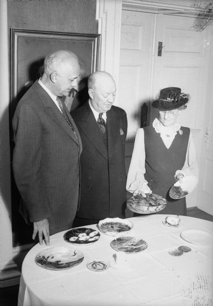 Two men and one woman look at dishes or plates donated to the Wisconsin Historical Society.