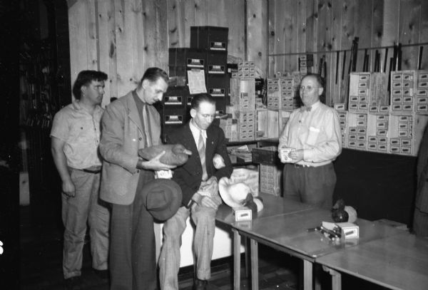 Three men and one salesman looking at duck decoys and buying shotgun shells inside Berg Sporting Goods Store, 2123 Atwood Avenue.