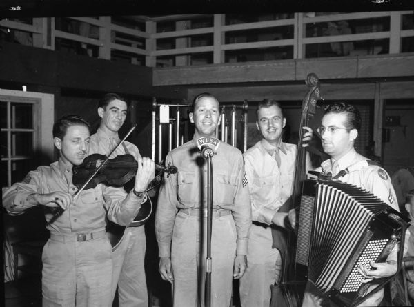 Truax Field soldiers produce a weekly radio show, "Truax Field Calling" for WIBA, broadcasting from the field. Shown performing at the microphone, left to right, are: Sgt. Joseph De Salvo, Corp. Lloyd Daigle, Sgt. Ed Singer, Corp. Reimer Hoffman and Corp. Armand Tosetti.