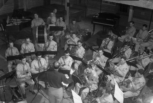 Truax Field soldiers produce a weekly radio show, "Truax Field Calling" for WIBA, broadcasting from the field. The band is shown from the balcony at the Service Club.