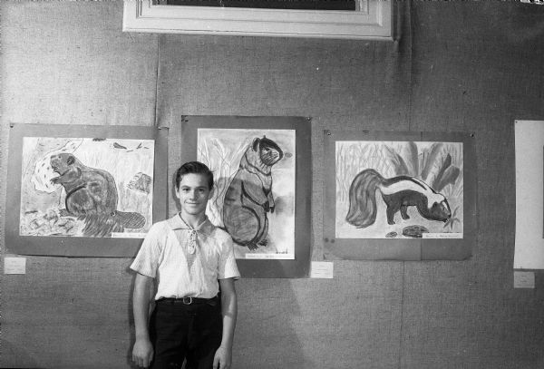 Alford Beckwith, seventh grade student at Longfellow School, with three of his animal paintings exhibited in the "Children Look at Wisconsin" exhibition at the Gregory Room of the State Historical Society. The exhibit features pictures selected from bi-monthly exhibitions held in the children's room of the Wisconsin Historical Museum throughout the past year.