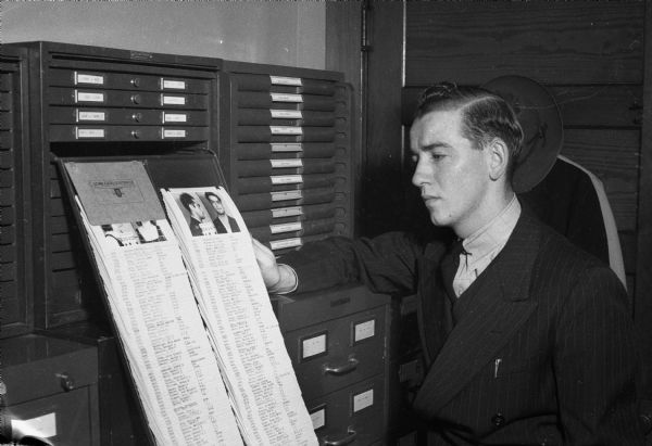 Edward Marr, bank messenger for Montgomery Ward and Co., and victim of Madison's second daylight holdup in a month, is searching through the bandit pictures in the police identification bureau to try to identify the two bareheaded bandits who robbed him of $4,910 of receipts from the Montgomery Ward and Co. store.