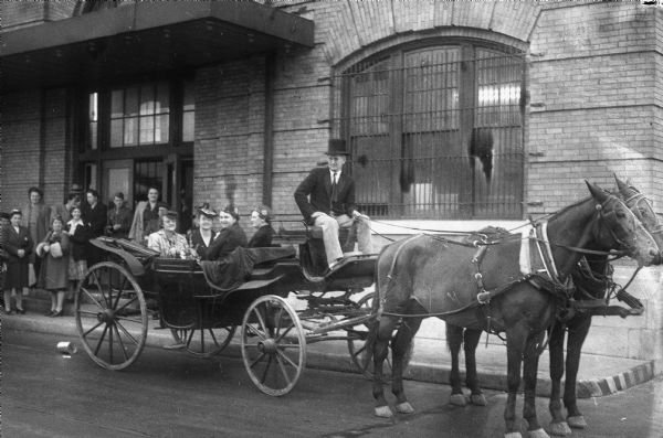 Four members of the Veterans of Foreign Wars Auxiliary, including Mrs. Hazel Miller, the national president, in a horse-drawn carriage in front of the Chicago, Milwaukee, St. Paul and Pacific Railroad depot. The building is located at 640 West Washington Avenue.