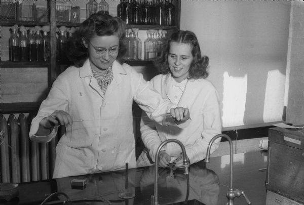 Barbara Baird (left,) and Mary Ellen Sperle are drawing a pipette from molten glass in a University of Wisconsin Laboratory. Traditionally, this work was done exclusively by men before World War II.