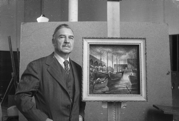 Portrait of University of Wisconsin Art Education professor Roland S. Stebbins with one of his paintings, which he donated to the Madison Art Association for them to sell to raise money for their own benefit.